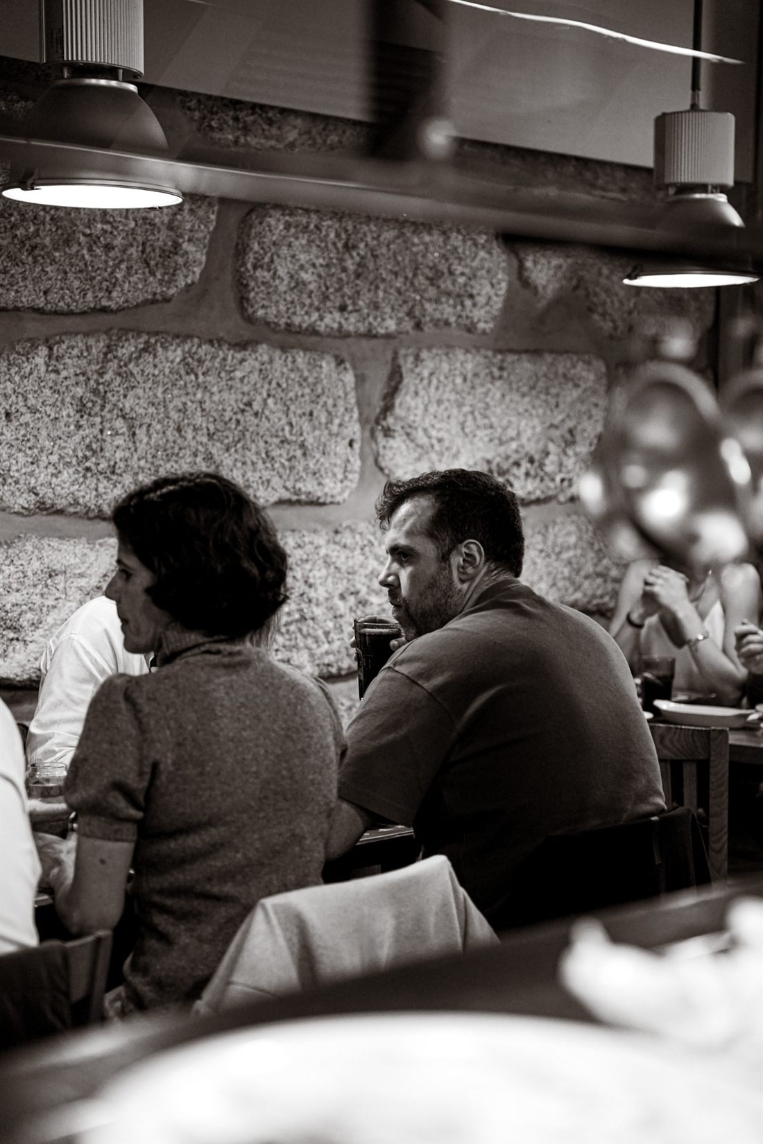 Two diners at a table in the granite-walled room at Capa na Baixa, black and white