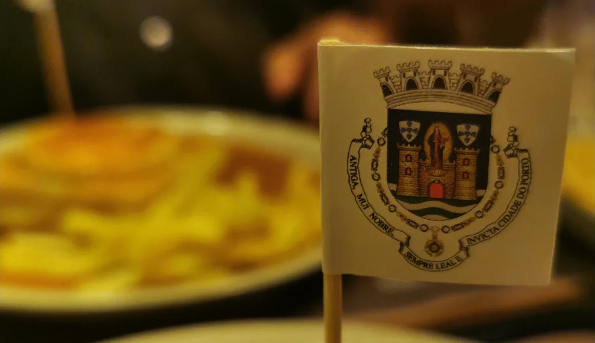 A francesinha topped with a small paper flag showing the coat of arms of Porto